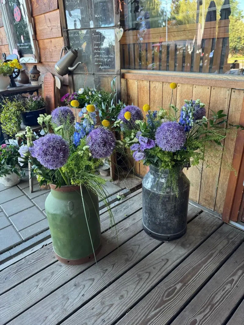 Milchkannen mit Allium und Wiesenblumen auf der Terrasse